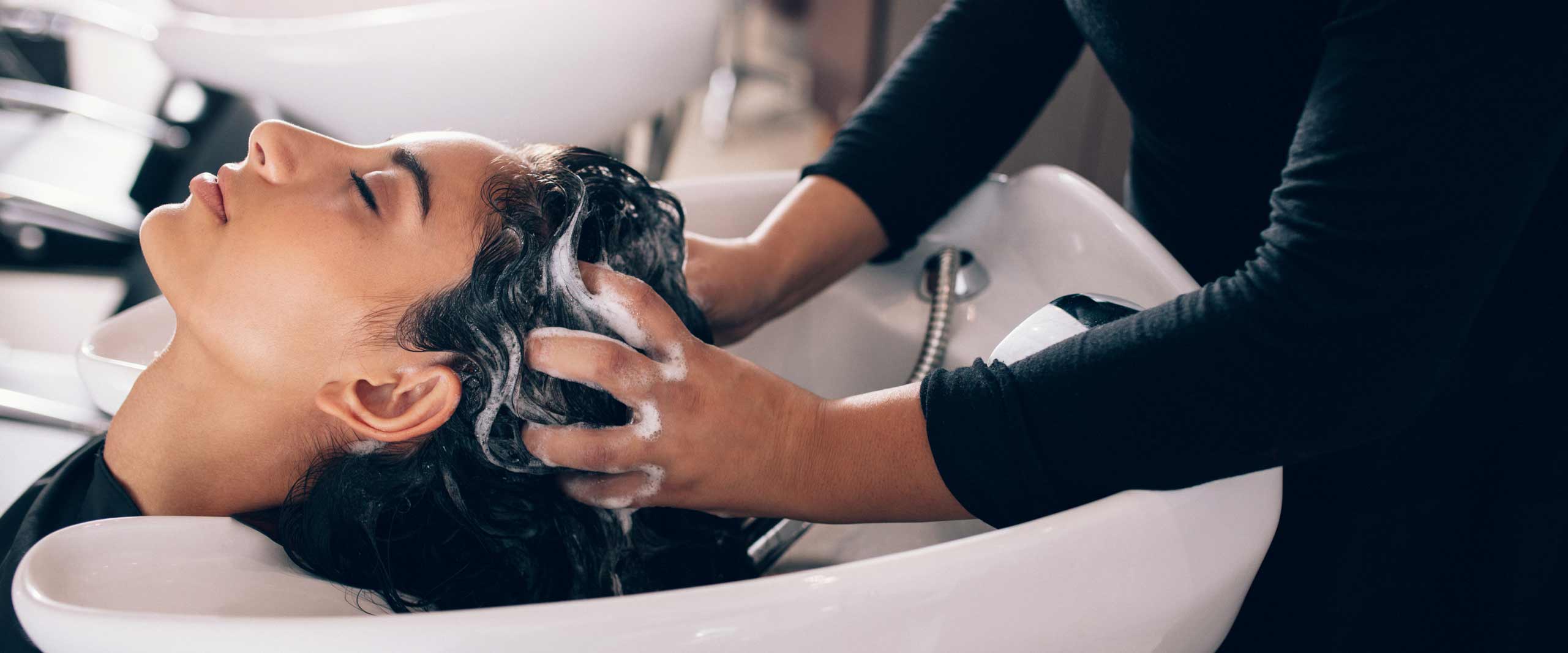 A client relaxing while a stylist massages shampoo through her hair
